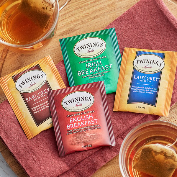 A variety of Twinings black tea bags on a table with a green packet of tea.