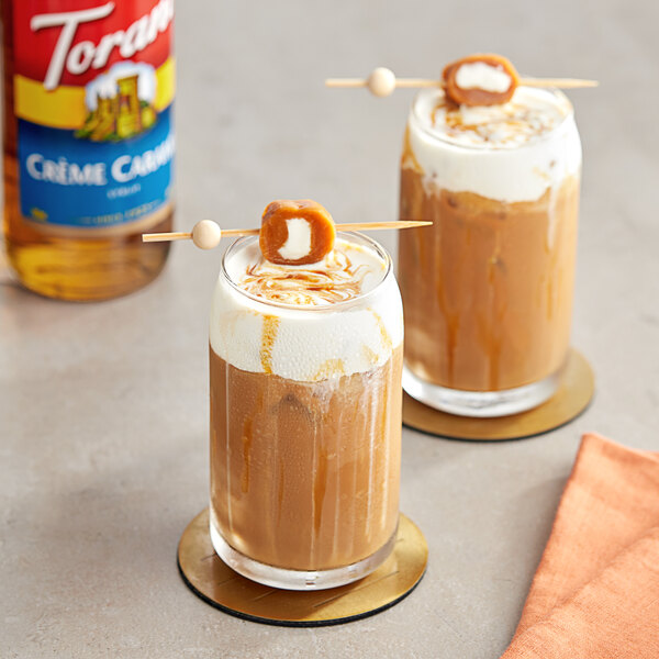 Two glasses of brown liquid with a marshmallow on top using Torani Creme Caramel Flavoring Syrup.