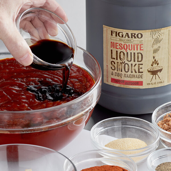 A hand pouring Figaro mesquite liquid into a bowl of barbecue sauce.