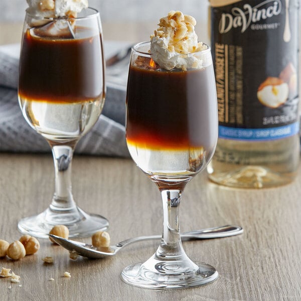 A close-up of a glass of brown liquid with whipped cream and nuts.