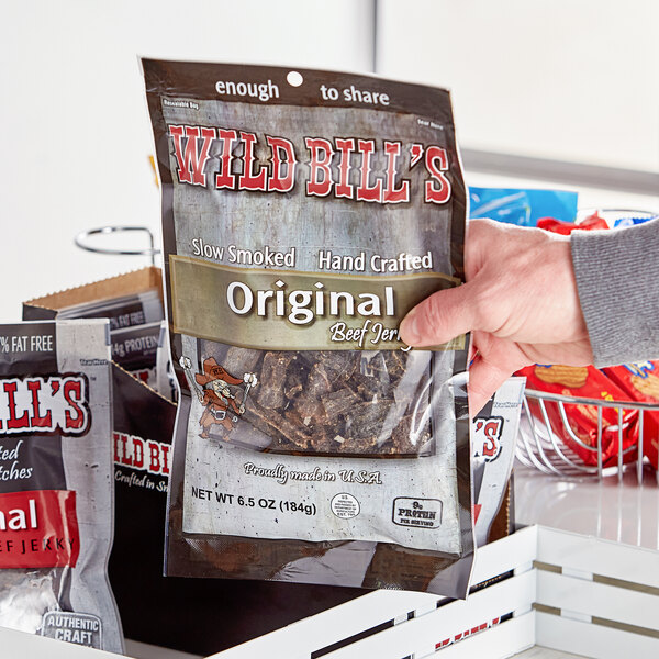 A hand holding a box of Wild Bill's hickory-smoked beef jerky.