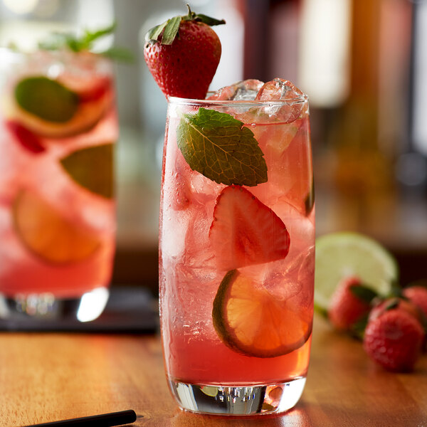 A glass of pink strawberry drink with strawberries and limes on a table.