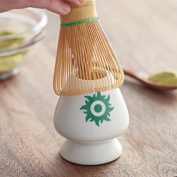 A hand holding a Tenzo porcelain matcha whisk over a white cup.