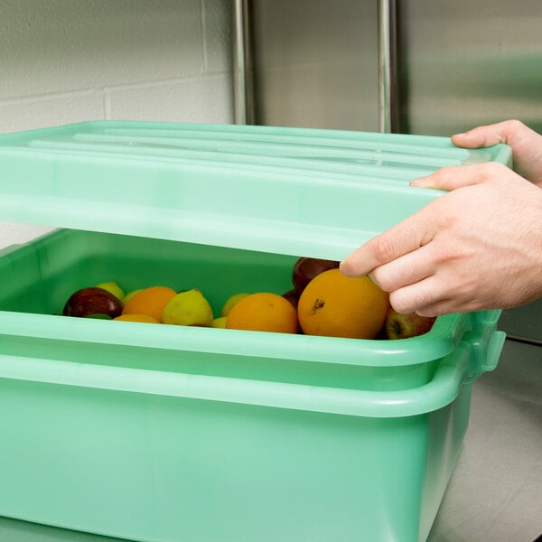 A hand opening a Vollrath Traex food storage box lid to reveal fruit inside.