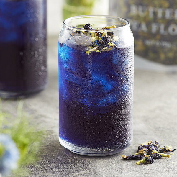 A glass of blue butterfly flower tea with ice and dried hibiscus flowers on the table.
