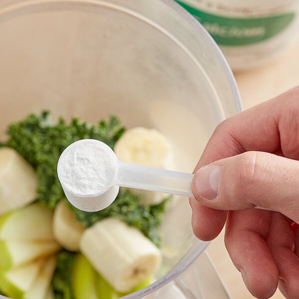 A hand using a measuring spoon to add Add A Scoop Calcium Blend supplement powder to a blender.
