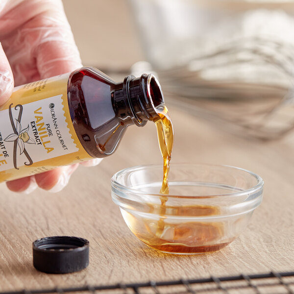 A hand pouring LorAnn Oils Pure Vanilla Extract into a glass bowl.