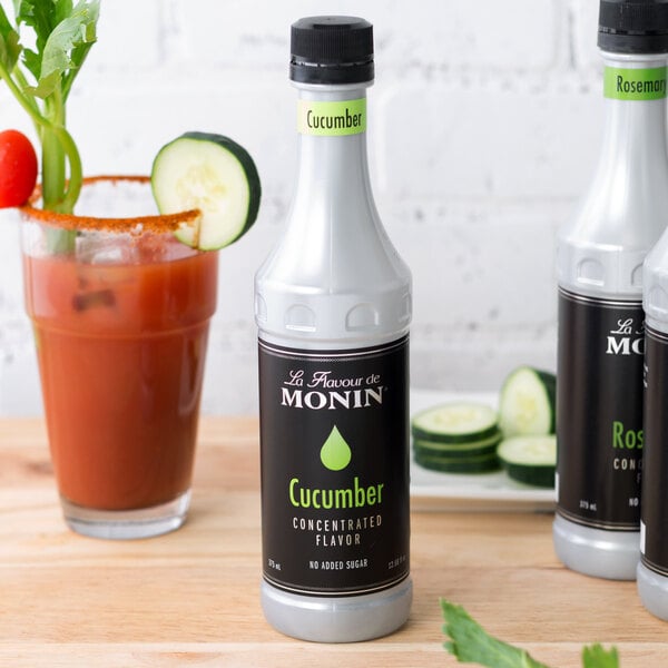 A white Monin bottle with black and green text and a close up of a cucumber.