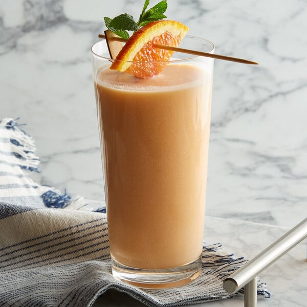 A glass of orange liquid with a straw and fruit on top.