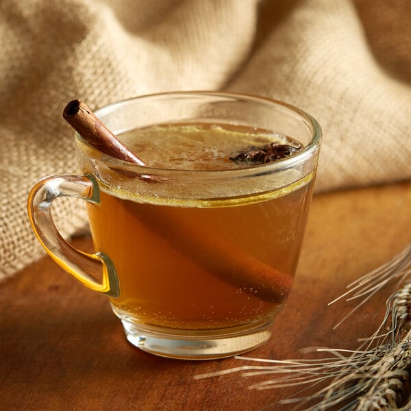 A glass cup of brown DaVinci Gourmet tea with a cinnamon stick.