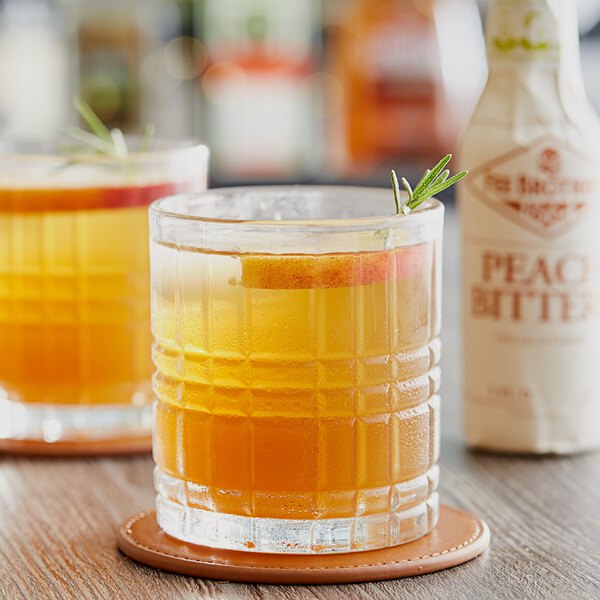 A glass of liquid with a sprig of rosemary on a coaster.