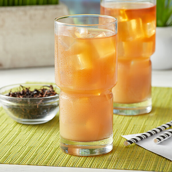 A glass of ice tea with orange liquid and ice on the side.