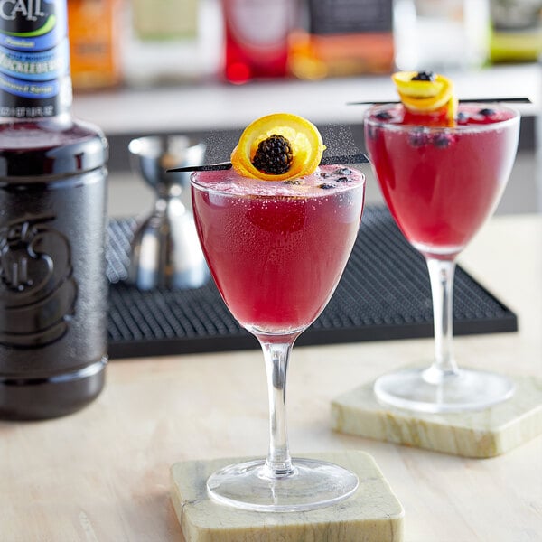 A glass of red cocktail made with Finest Call Wild Mountain Huckleberry Syrup on a table in a cocktail bar.