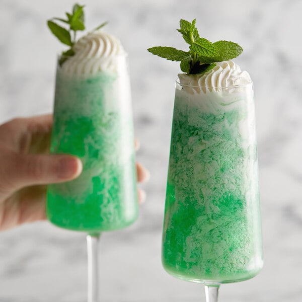 Two glasses of green and white DaVinci Gourmet peppermint drinks with mint leaves.