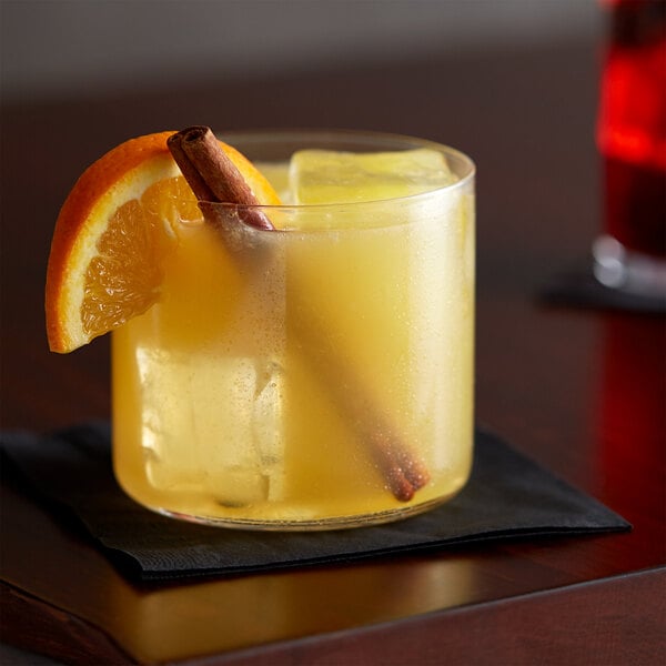 A glass of yellow liquid with an orange slice and a cinnamon stick on a table.
