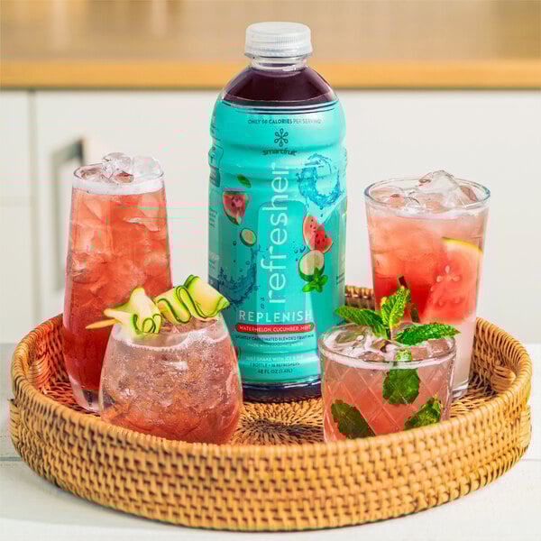 A basket with a glass of pink Smartfruit Replenish drink with ice and mint leaves on a table.