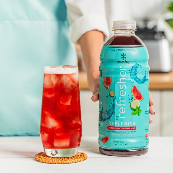 A person holding a bottle of Smartfruit Watermelon Cucumber Mint refresher next to a glass of liquid.