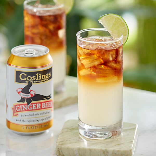 A glass of iced tea with a lime wedge and a can of Goslings Ginger Beer on a white table.