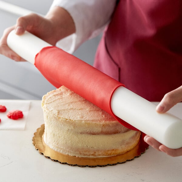 A person using a roll of red Satin Ice ChocoPan to cover a cake.