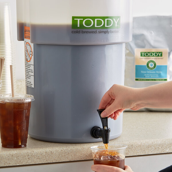 A person pouring Toddy New Orleans Style cold brew coffee into a glass from a dispenser.