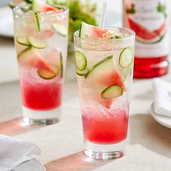 A glass of Monin watermelon and cucumber drink with cucumber slices and a straw.