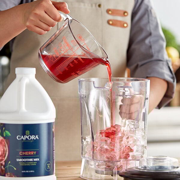 A person pouring Capora Cherry fruit smoothie mix into a blender.