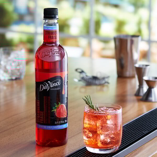 A bottle of DaVinci Gourmet sugar free strawberry syrup next to a glass of red liquid with ice.