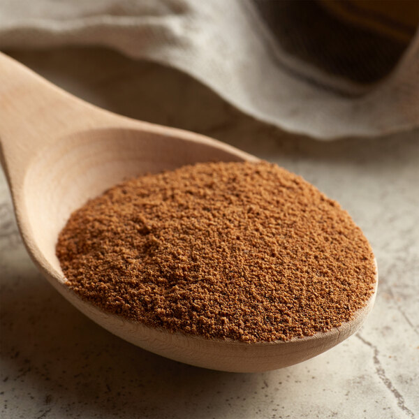 A wooden spoon filled with brown ground nutmeg on a table.