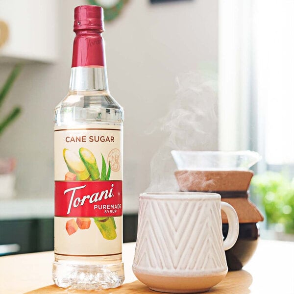 A Torani Puremade Pure Cane Sugar syrup bottle next to a cup of coffee.