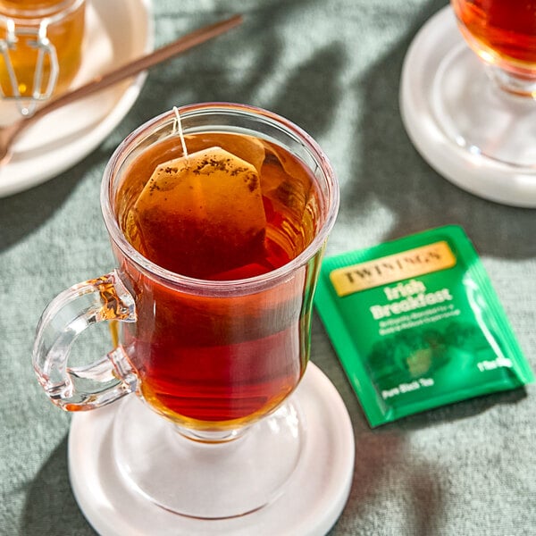 A glass mug of Twinings Irish Breakfast Tea with a tea bag in it.