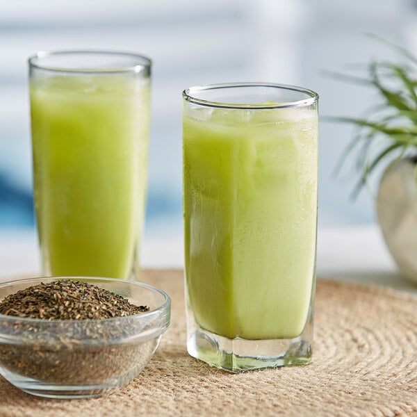 A glass of green ChaTraMue Thai milk tea next to a bowl of green seeds.