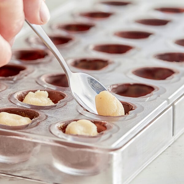 A hand using a spoon to put almond paste into a plastic container with small round holes.