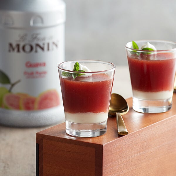 Two glasses of red guava juice with leafy green garnishes on a wooden tray.