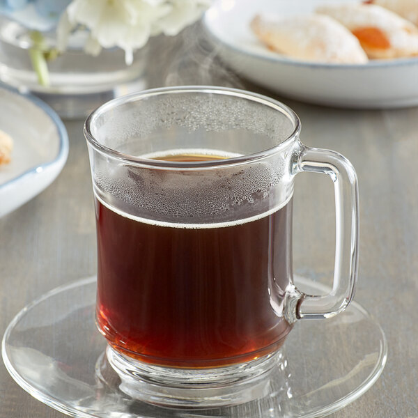 A saucer with a glass mug of brown Caffe de Aroma decaf coffee on it.