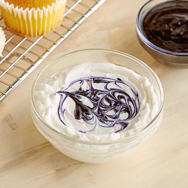 A bowl of chocolate frosting with a cupcake on top with purple and white swirled frosting.