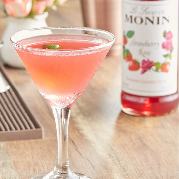 A glass of pink liquid with a green leaf on top sitting on a table.