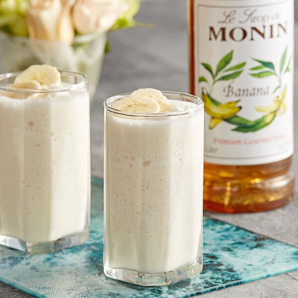 Two glasses of white liquid flavored with Monin banana syrup.