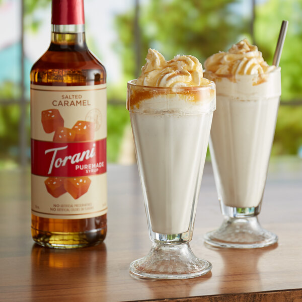 A bottle of Torani Puremade Salted Caramel flavoring syrup next to a glass of milk.