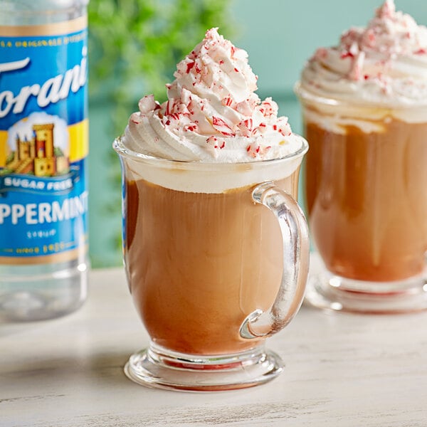 A glass mug of coffee with whipped cream and Torani Sugar-Free Peppermint Syrup with peppermint on top.