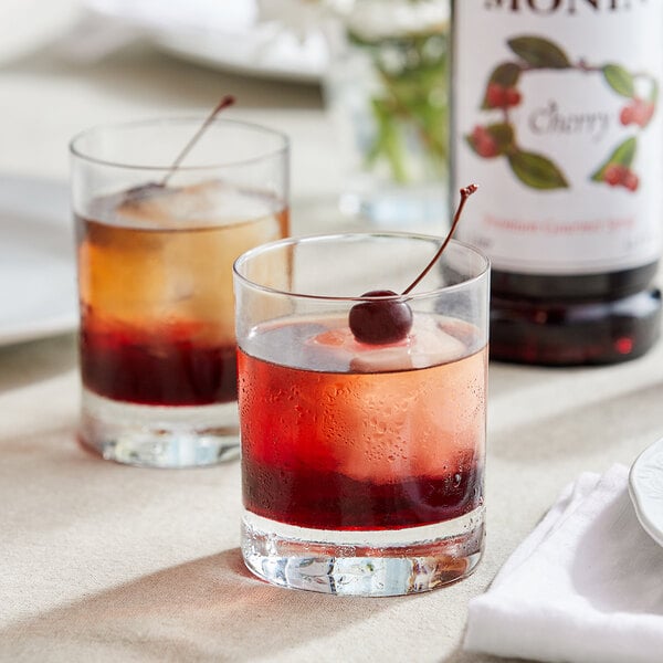 Two glasses of liquid with Monin Cherry Syrup and a cherry on top.