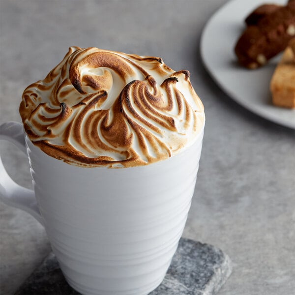 A white mug of coffee with whipped cream and a brown and white swirly top.