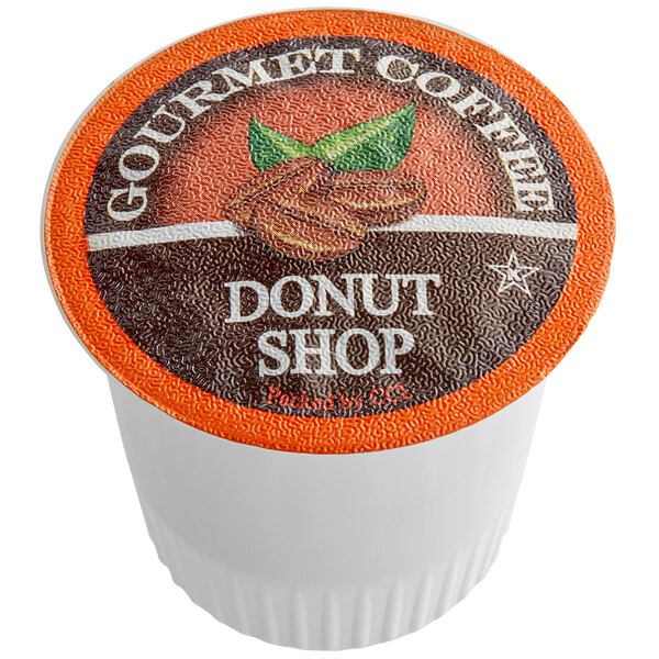 A white and orange Caffe de Aroma container of Donut Blend coffee single serve cups on a counter.