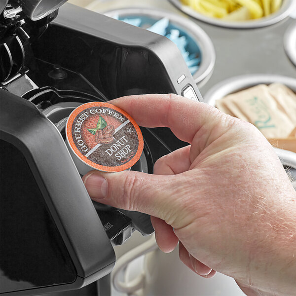 A hand holding a round Caffe de Aroma Donut Blend coffee cup with a black lid.