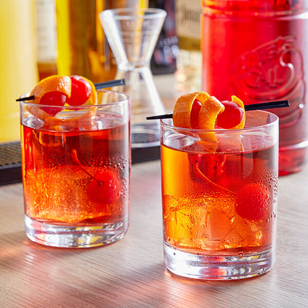 Two glasses of drinks with cherry garnishes on a table.