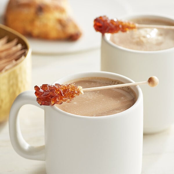 A white mug of coffee with a brown sugar stick in it.