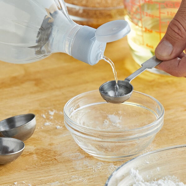 A person pouring McCormick Imitation Almond Extract into a metal ladle over a bowl.