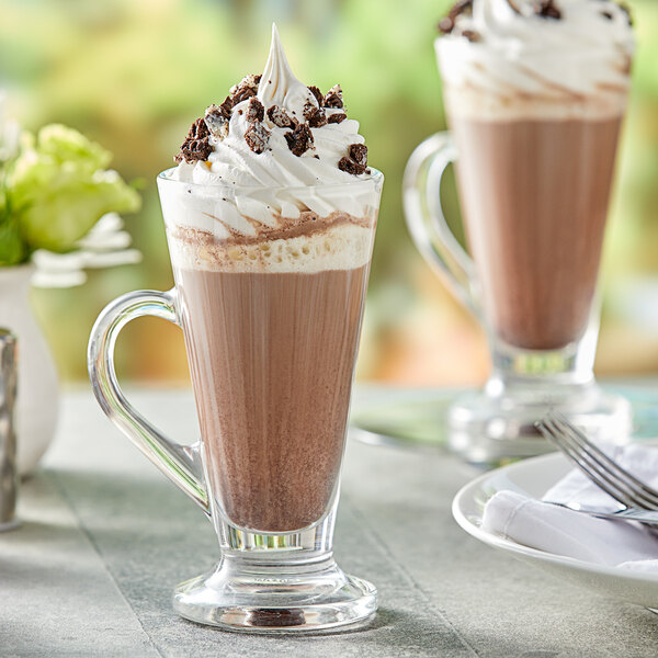 A glass of Capora Cookies & Cream Frappe mix with whipped cream and chocolate chips on a table.