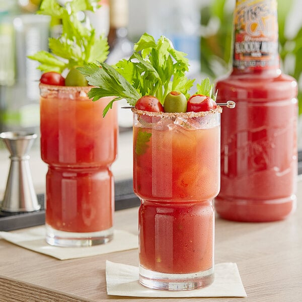 Two glasses of Bloody Mary with a garnish on a table.