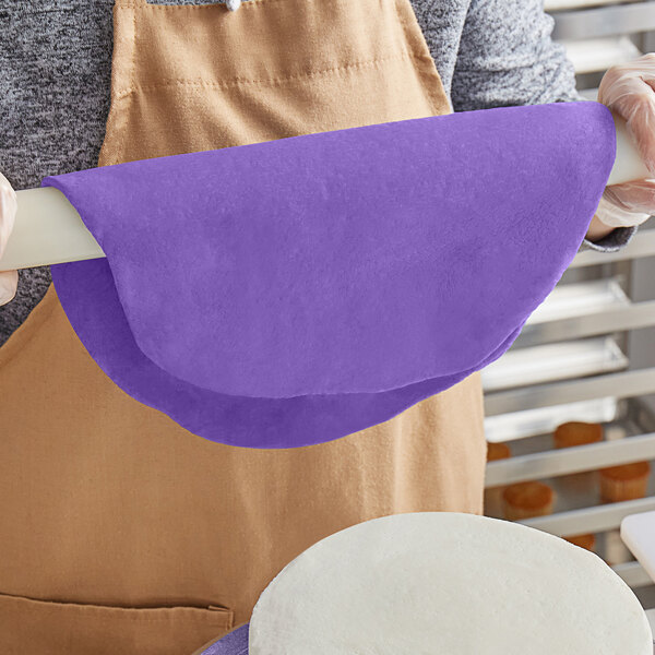 A person rolling out purple Satin Ice chocolate-flavored rolled fondant with a purple rolling pin on a white surface.