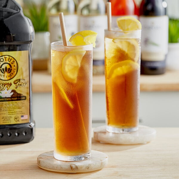 A pair of glasses of Lotus Plant Energy Naturally Sweetened Tea with lemon slices and a straw.